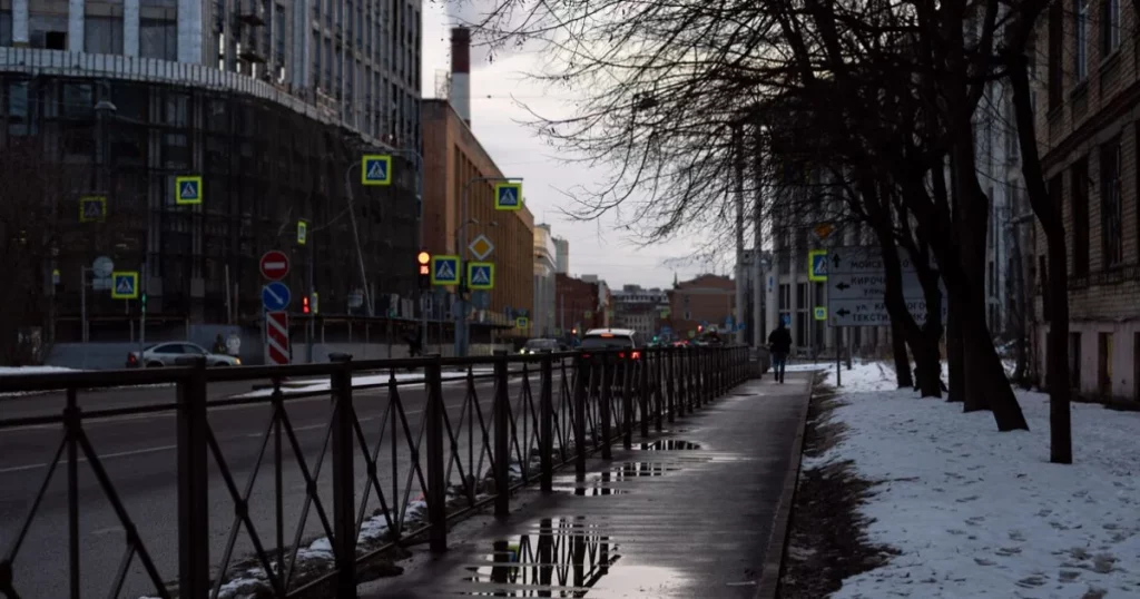City street in winter with snow and reflections on wet sidewalk and street.