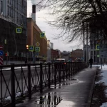City street in winter with snow and reflections on wet sidewalk and street.