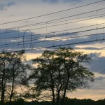 Scenic view of transmission towers and trees silhouetted at sunset in rural countryside.